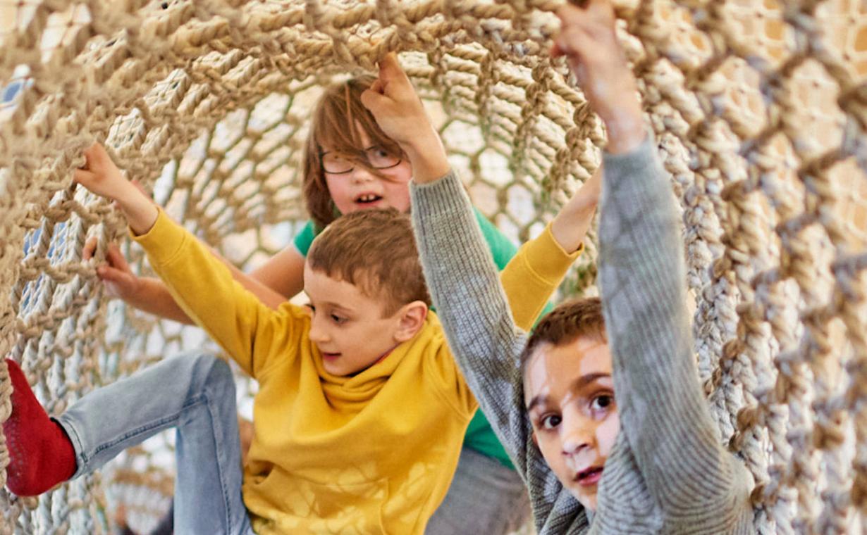 drei Kinder in einem Klettertunnel aus Seilen