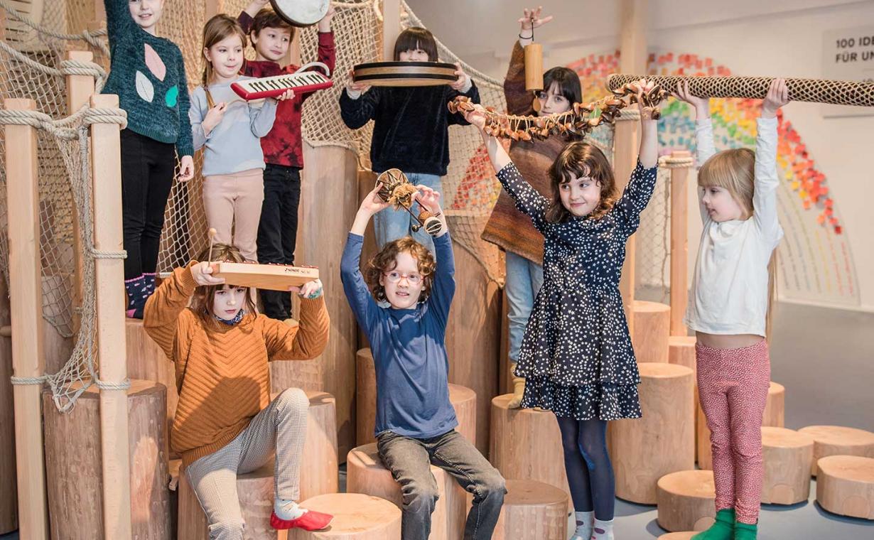 Das Bildzeigt eine Gruppe von Kindern, die Gegenstände in die Luft halten. 