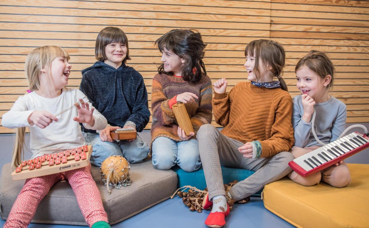 F&uuml;nf Kinder sitzen mit unterschiedlichen Instrumenten auf dem Boden .