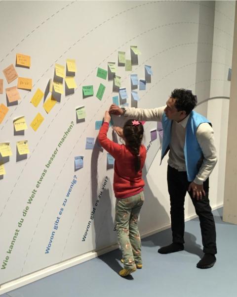 A man and a child stand in front of a wall with stickynotes