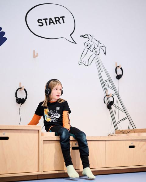 Kind sitzt mit Kopfhörern auf einem Möbelstück.