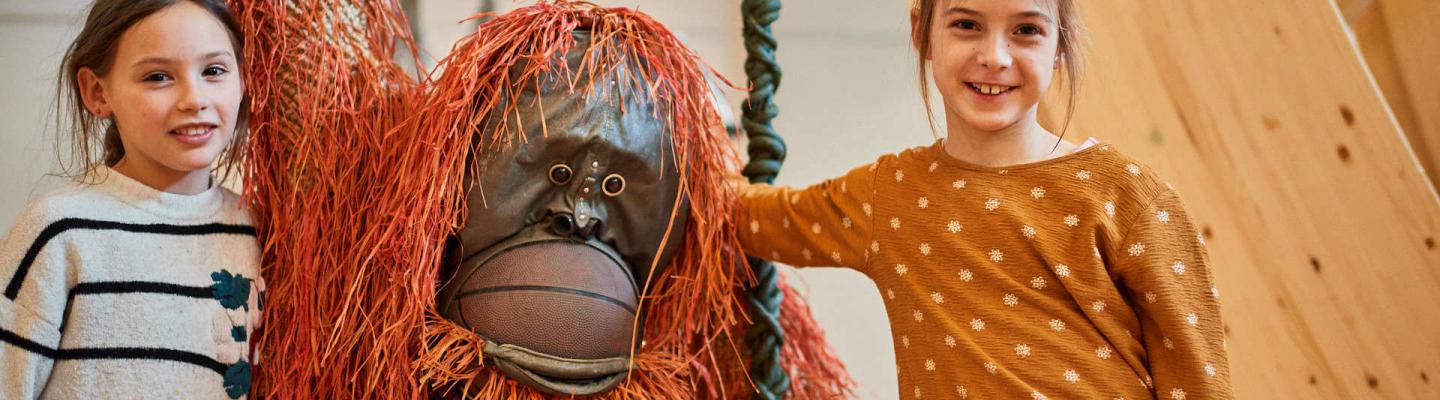 Zwei Kinder umarmen die Orang-Utan Tierskulptur 