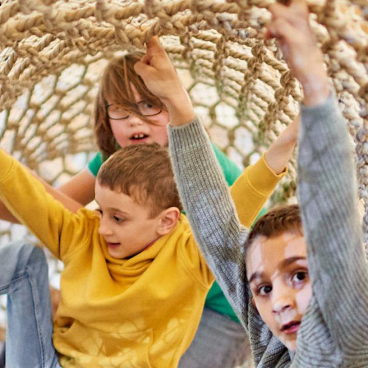 drei Kinder in einem Klettertunnel aus Seilen