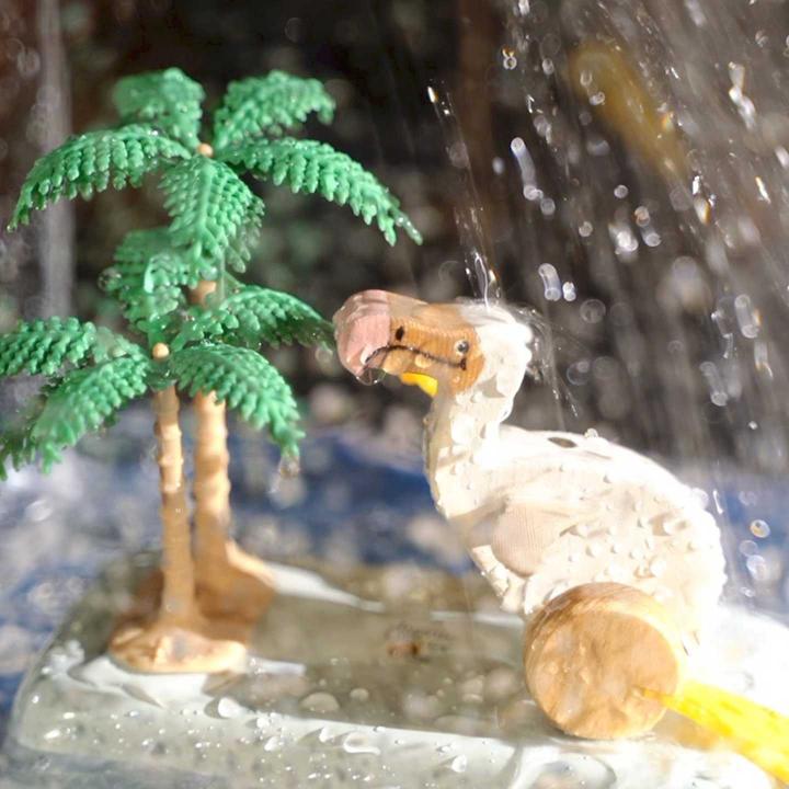 Toy animal next to toy palm trees standing in the rain.
