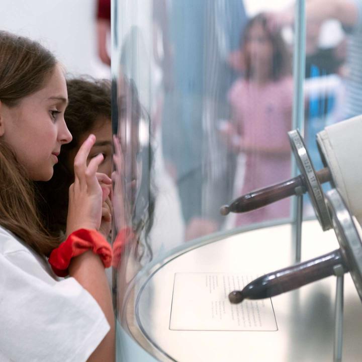 Two children are looking at a Torah scroll that is behind a curved glass panel.