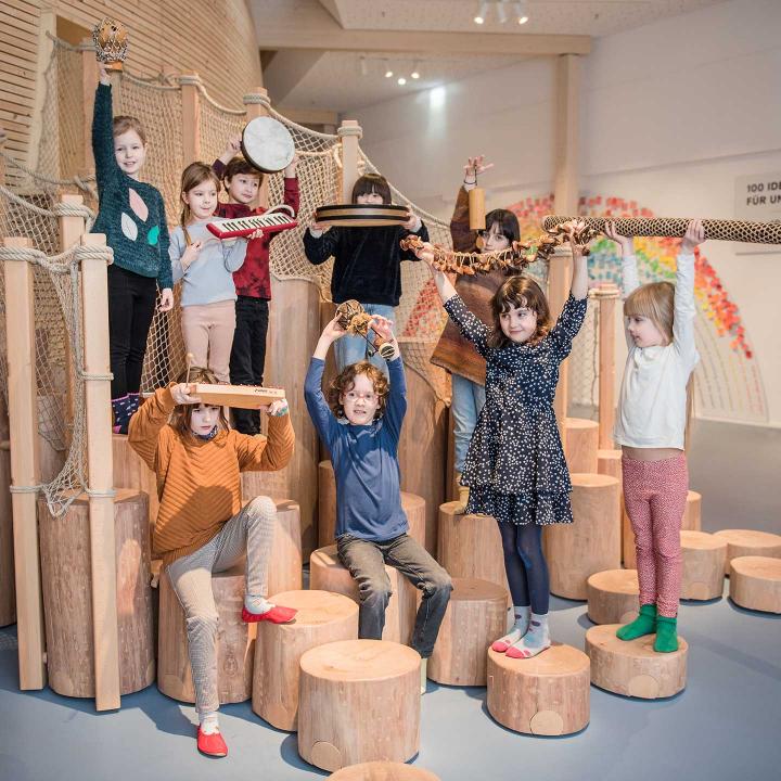 Das Bildzeigt eine Gruppe von Kindern, die Gegenstände in die Luft halten. 